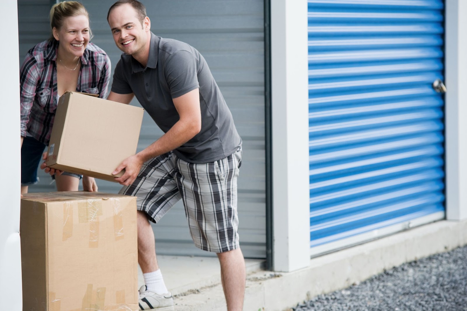 A man and a woman smiling while carrying boxes in a storage facility